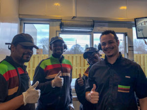 Happy Burger King employees around drive-thru window air curtain.