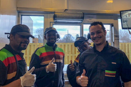 Happy Burger King employees around drive-thru window air curtain.